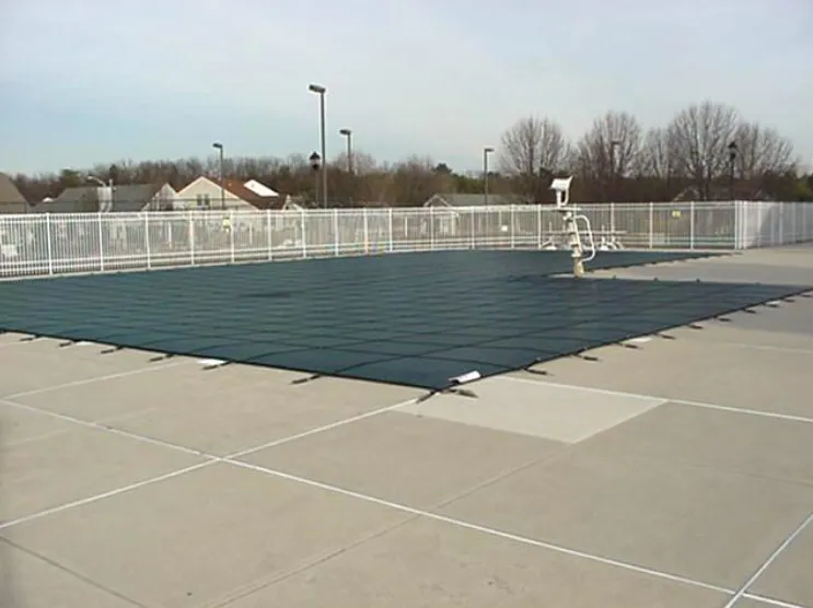Large commercial pool with green safety cover, lifeguard stand, and expansive concrete deck behind a white aluminum fence in Lakehurst, NJ by Gorlin Pools