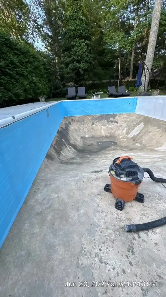 Drained pool interior with new blue wall panels and wet vacuum on the concrete floor during daytime liner replacement preparation in Lakehurst, NJ by Gorlin Pools