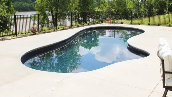 Freeform fiberglass pool with volcanic black finish and smooth concrete deck next to a waterfront property in Lakehurst, NJ by Gorlin Pools