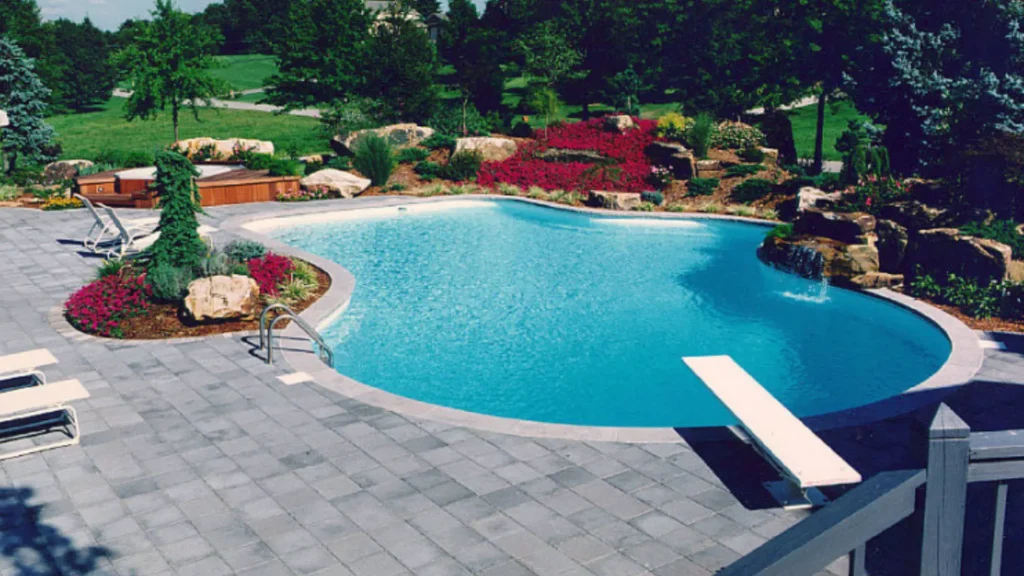 Freeform in-ground pool with diving board, paver patio, and rock waterfall feature in a landscaped backyard in New Jersey by Gorlin Pools