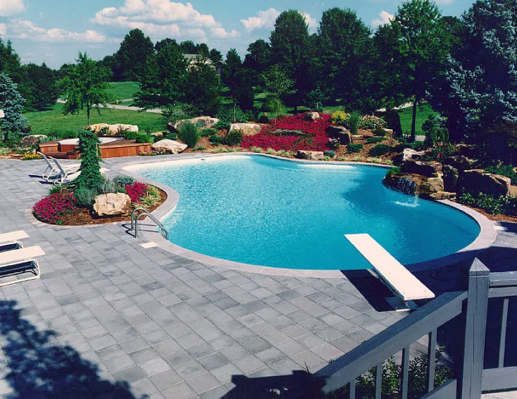 Freeform in-ground pool with diving board, paver patio, and rock waterfall feature in a landscaped backyard in New Jersey by Gorlin Pools