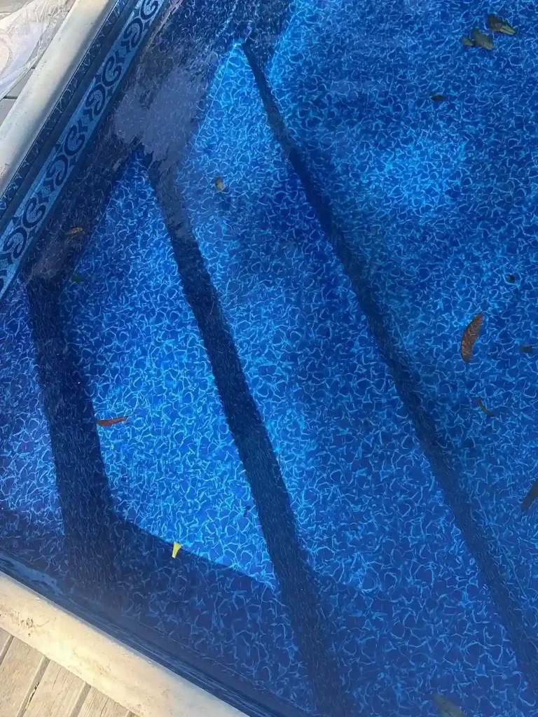 Close-up of lifted and wrinkled vinyl liner pulling away from pool steps with scattered leaves showing replacement is needed in Lakehurst, NJ by Gorlin Pools