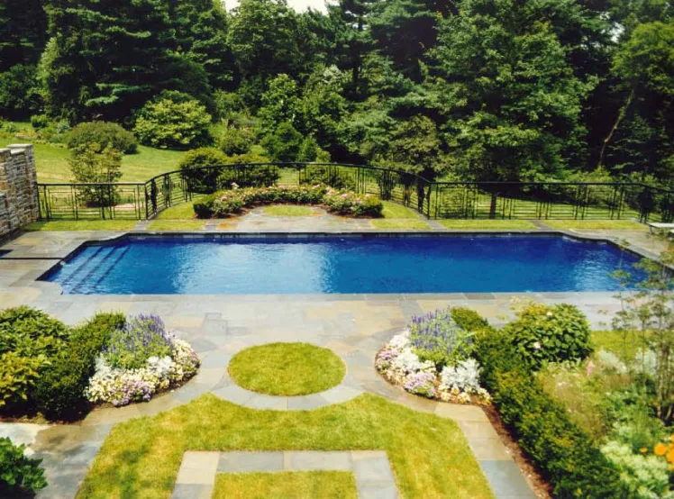 Rectangular in-ground pool with bluestone coping, wrought iron fence, and manicured flower beds in New Jersey by Gorlin Pools