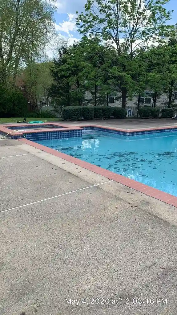 Rectangular pool with attached spa, blue tile accent, brick coping, and exposed aggregate concrete deck during spring opening in Lakehurst, NJ by Gorlin Pools