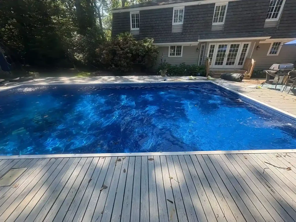 Rectangular pool with dark blue vinyl liner being filled next to a wood deck and shingle colonial home in Lakehurst, NJ by Gorlin Pools
