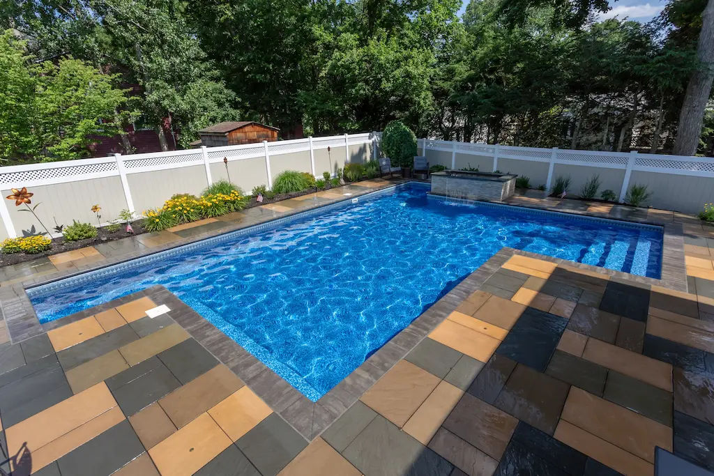 Rectangular vinyl pool with patterned flagstone deck, white privacy fence, and flower garden in Lakehurst, NJ by Gorlin Pools