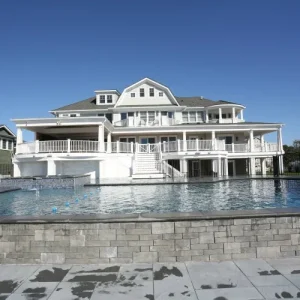 Commercial pool with stone retaining wall and large white coastal resort building in the background in Lakehurst, NJ by Gorlin Pools
