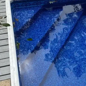 Severely wrinkled and damaged vinyl liner inside a pool before replacement, with leaves and equipment on the wood deck in Lakehurst, NJ by Gorlin Pools