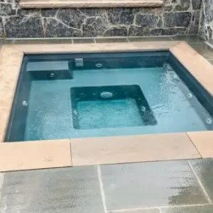 Fiberglass in-ground spa with silver finish, jet seats, and bluestone coping set inside a natural stone wall enclosure in Lakehurst, NJ by Gorlin Pools