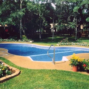 Figure-eight shaped pool with blue vinyl liner, concrete apron, and colorful flower garden beds in a wooded backyard in Lakehurst, NJ by Gorlin Pools