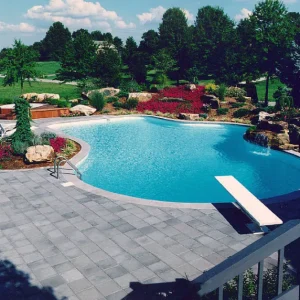 Freeform in-ground pool with diving board, paver patio, and rock waterfall feature in a landscaped backyard in New Jersey by Gorlin Pools