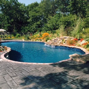 Freeform pool with dark vinyl liner, natural rock waterfall, colorful flower garden, and stamped concrete patio in Lakehurst, NJ by Gorlin Pools
