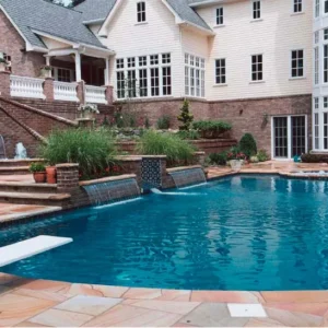 Freeform pool with diving board, brick waterfall walls with tile accents, and sandstone patio at a grand manor home in Lakehurst, NJ by Gorlin Pools