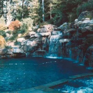 Freeform pool with a large natural boulder waterfall wall and wooded hillside backdrop in New Jersey by Gorlin Pools