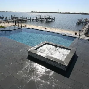 Geometric pool with raised square glass tile spa and dark slate paver deck overlooking a waterfront marina in Lakehurst, NJ by Gorlin Pools
