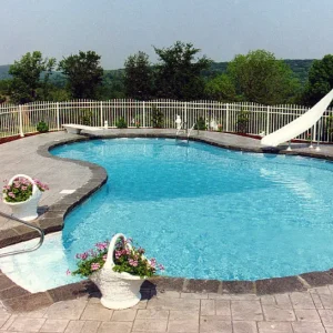 Kidney-shaped pool with diving board, white water slide, stamped concrete patio, and rolling hillside view in Lakehurst, NJ by Gorlin Pools