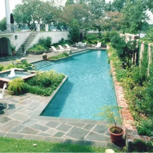 Lap pool with a square fountain feature, brick retaining wall, and bluestone patio at a Mediterranean-style estate in Lakehurst, NJ by Gorlin Pools