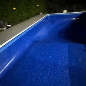 Corner angle view of a newly installed blue vinyl liner in an empty rectangular pool being filled at night in Lakehurst, NJ by Gorlin Pools