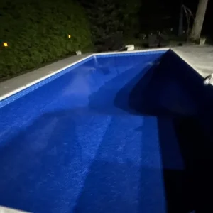Newly installed blue vinyl liner in a rectangular pool lit by underwater lighting at night in New Jersey by Gorlin Pools