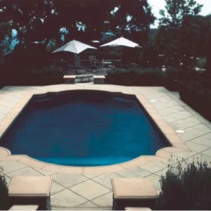 Octagonal pool with dark plaster finish and scalloped sandstone coping on a formal patio with market umbrellas at dusk in Lakehurst, NJ by Gorlin Pools