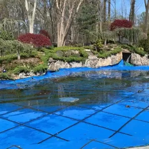 In-ground pool with blue mesh safety cover ready for spring opening on a flagstone patio in New Jersey by Gorlin Pools