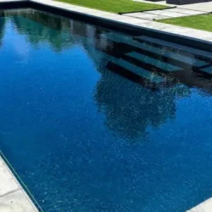 Rectangular fiberglass pool with dark finish, wide built-in entry steps, and modern concrete coping surround in Lakehurst, NJ by Gorlin Pools