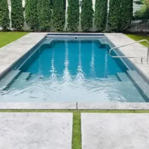 Rectangular fiberglass pool with gray finish, stainless steel handrail, and concrete paver surround with grass strips in Lakehurst, NJ by Gorlin Pools