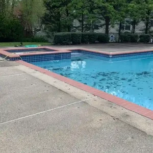 Rectangular pool with attached spa, blue tile accent, brick coping, and exposed aggregate concrete deck during spring opening in Lakehurst, NJ by Gorlin Pools