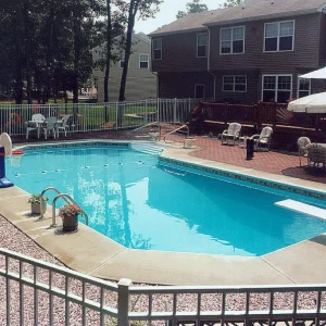 Rectangular pool with diving board, floating basketball hoop, white metal fence, and brick paver patio at a suburban home in Lakehurst, NJ by Gorlin Pools